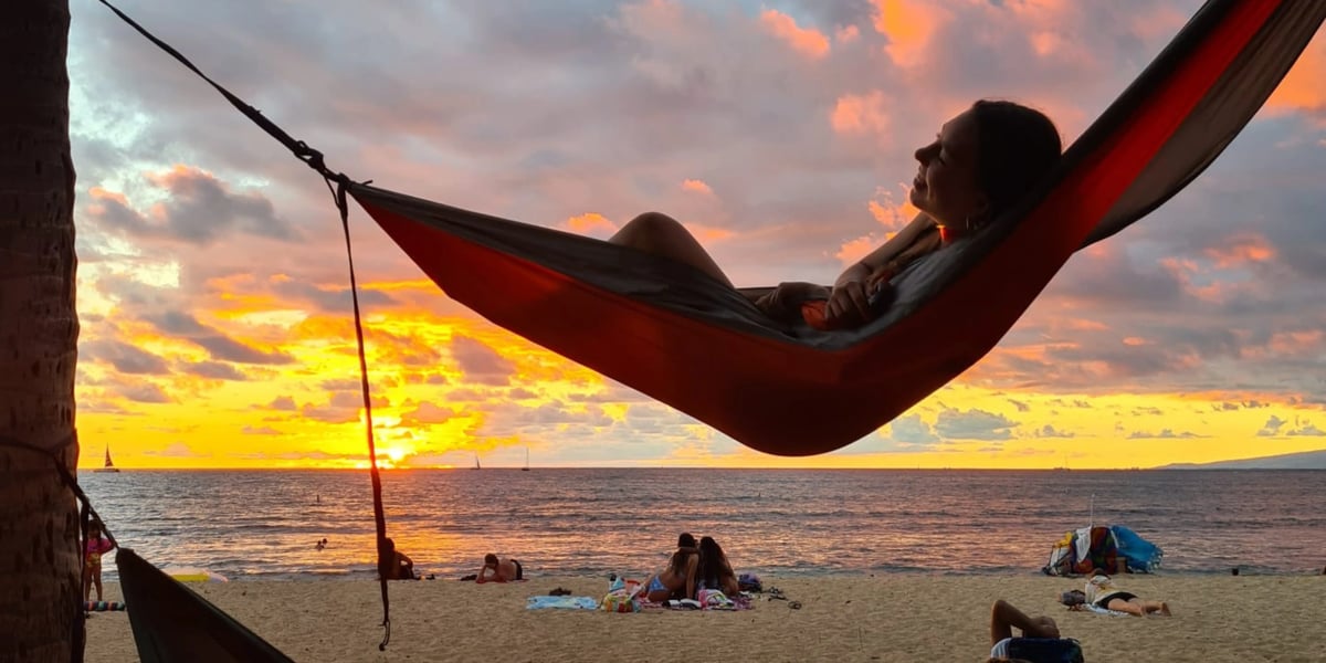 Studentin entspannt in einer Hängematte am Strand bei Sonnenuntergang.