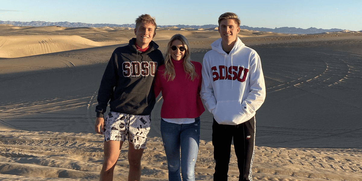 Drei Studierende posieren in der Wüste mit Hoodies der San Diego State University. 