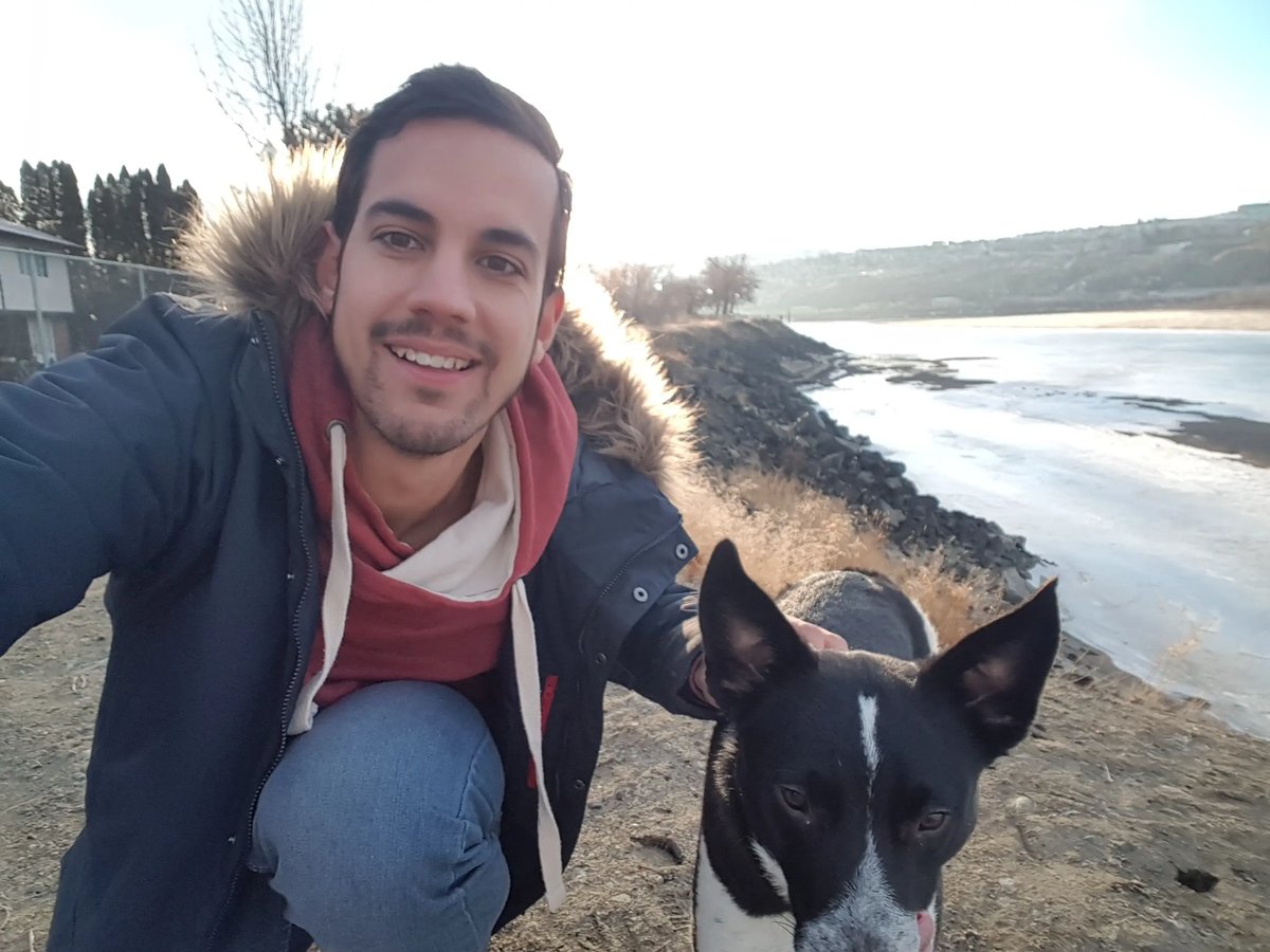 Junger Mann macht ein Selfie mit einem Hund an einem Flussufer.