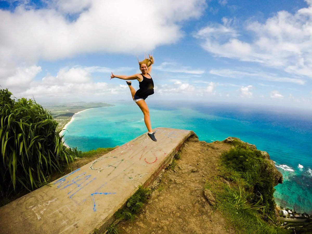 Junge Frau springt auf einem Aussichtspunkt mit Blick auf das Meer 